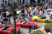 a group of people standing in front of a group of red sports cars