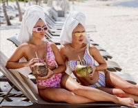 two women sitting on lounge chairs with coconuts in their hands